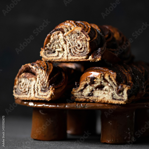 Babka with chocolate filling. Twisted sweet traditional Jewish pastries. Cross-sectional view, serving on platter, dark background.
