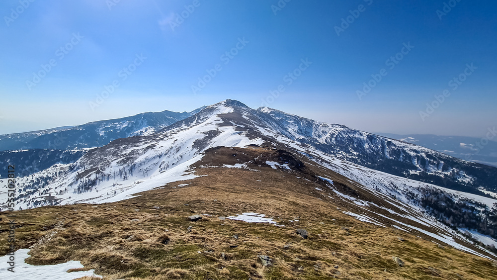 Fototapeta premium Ascent over snow covered alpine pasture to mountain peak Scharfes Eck near Zirbitzkogel, Seetal Alps, Styria (Steiermark), Austria, Europe. Idyllic hiking trail on ridges in sunny early spring