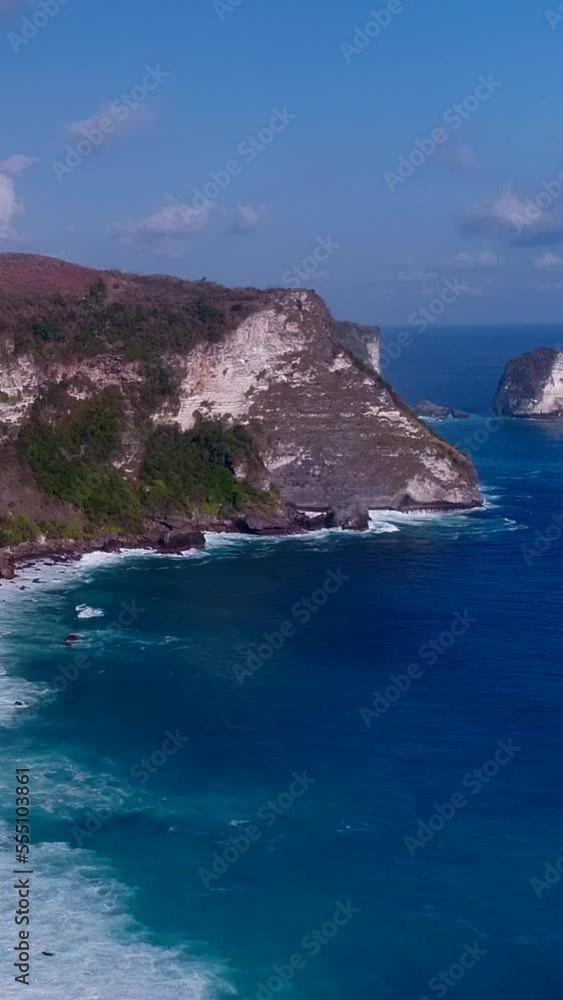 Vertical video of Aerial shot of rocky cliffs with waves breaking over shallow coral reef Vertical video of Aerial shot of rocky cliffs with waves breaking over shallow coral reef