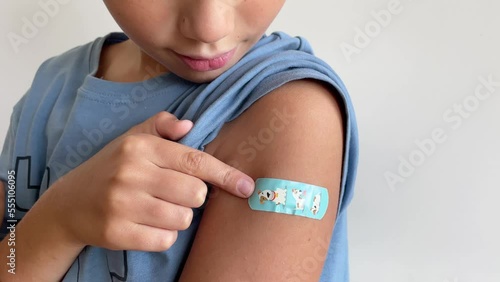 Child after vaccination with adhesive band-aid patch arm bandage to prevent any infection over white background. Positive concept of healthy lifestyle and care.