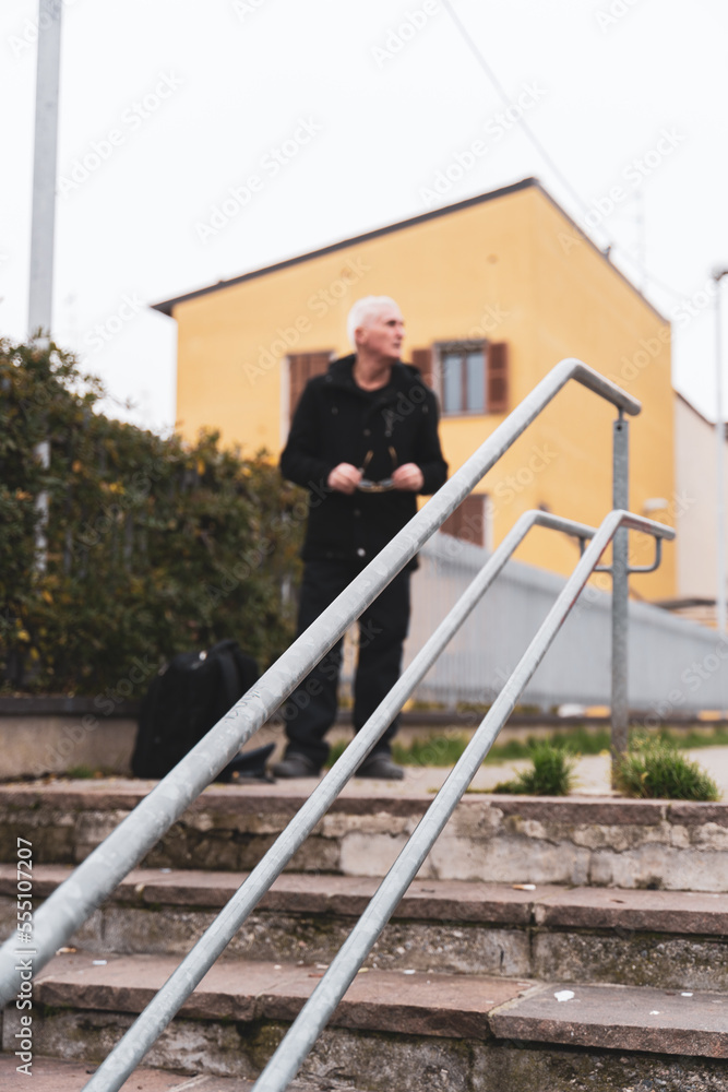 mature man rap singer posing on stairs outdoors on the outskirts of a city