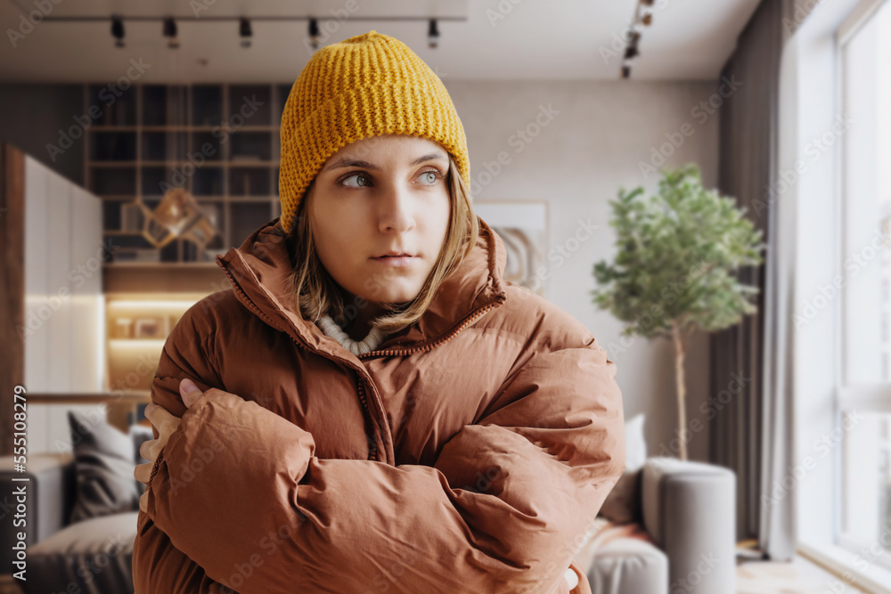 Woman in a warm down jacket trying to keep warm at home. Home heating shutdown concept. Gas shutdown. Woman in a warm down jacket trying to keep warm at home. Home heating shutdown concept. Gas shutdown.