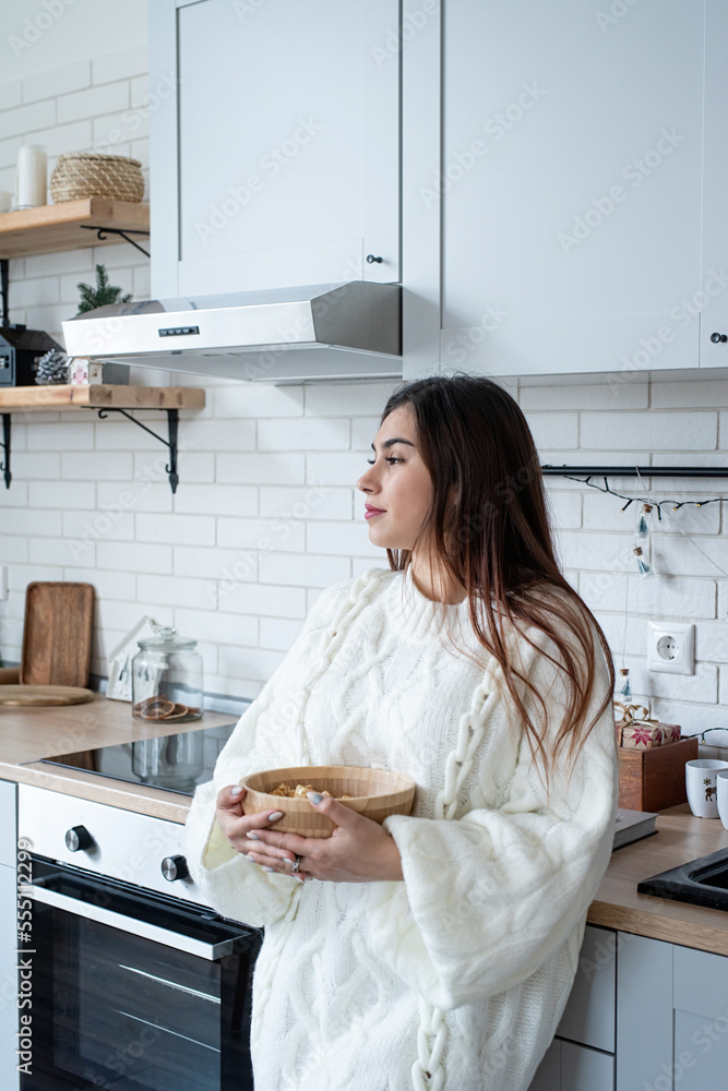 Woman in warm white winter sweater standing at the kitchen at home Woman in warm white winter sweater standing at the kitchen at home