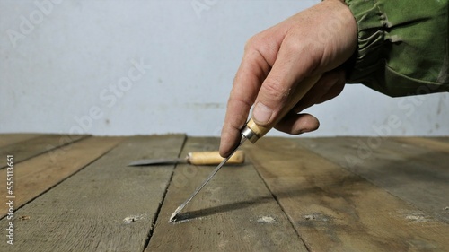 a hand with a narrow spatula covers with mastic small holes from a nail hammered into wood, smearing with a solution of cracks and holes on the surface of a wooden covering of a shelf or floor photo