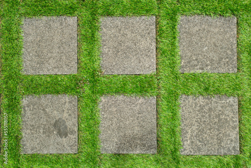 Flat lay shot of tile pavement close-up with artificial green grass. Abstract background texture.