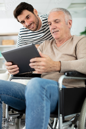 adult hipster son and senior father using tablet