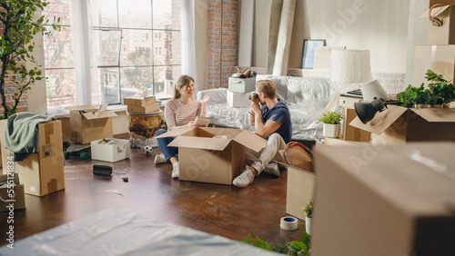 Happy Homeowners Moving In: Lovely Couple Sitting on the Floor of the Cozy Apartment Unpacking Cardboard Boxes, Taking Photos for Memories. Mortgage Loan, Real Estate. Nostalgia Cinematic Color