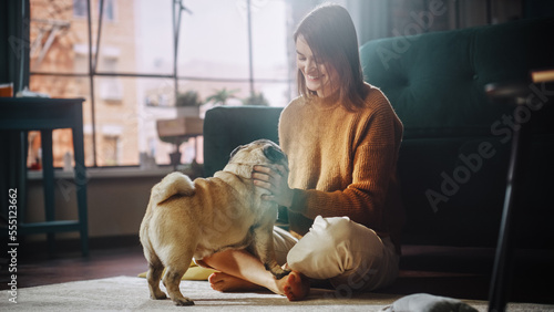Beautiful Young Woman Cuddles Her Adorable Little Pug at Home. Girl Plays with Her Dog, Gorgeous Pedegree Canine. She Teases, Pets and Scratches Super Happy Doggy, Have Fun in the Stylish Living Room. photo