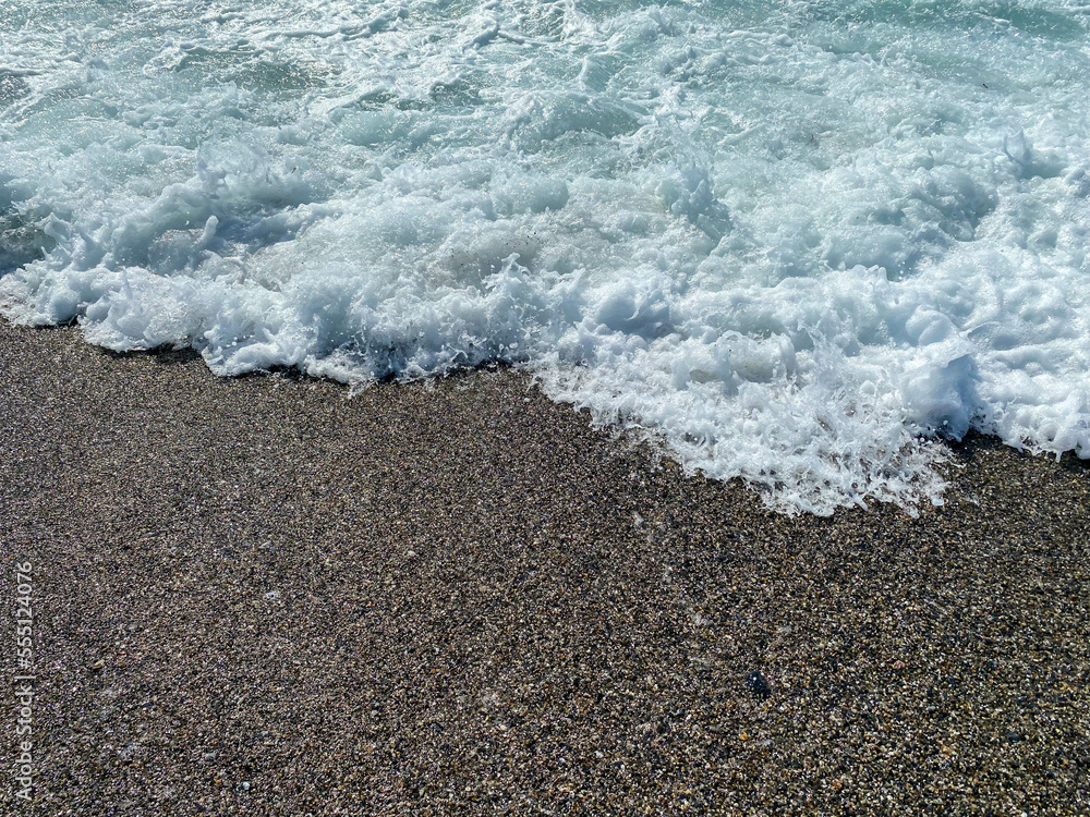 Waves of water in the sea and sand with small natural multi-colored stones on the seashore, small pebbles on the beach. Background, texture Waves of water in the sea and sand with small natural multi-colored stones on the seashore, small pebbles on the beach. Background, texture