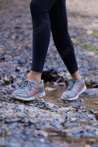 Woman, running shoes and feet in mud while hiking in nature for fitness, exercise and cardio training outdoor for health, travel and wellness on adventure. Legs of female athlete walking forest path © Lune V A/peopleimages.com