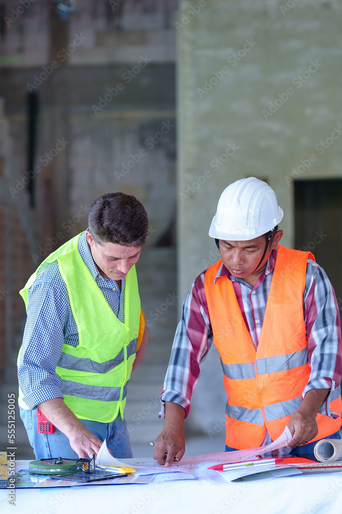 Two construction engineers holding blue print and inspecting the construction site Two construction engineers holding blue print and inspecting the construction site
