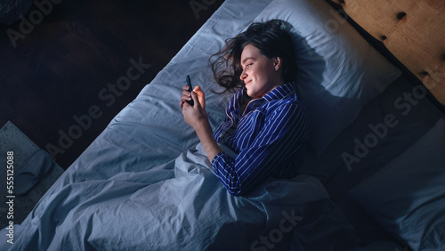 Top View Bedroom Apartment: Beautiful Young Woman Using Smartphone in Bed at Night. Smiling Girl Browsing Social Media, Romance in Dating Apps, Remote Work Software, Doing Internet Online Shopping