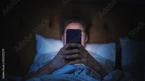 Anonymous Man Uses Smartphone in Bed at Home at Night. Handsome Guy Browsing Social Media, Reading News, Doing Online Shopping Late at Night. Focus on Hand Holding Mobile Phone Covering Face