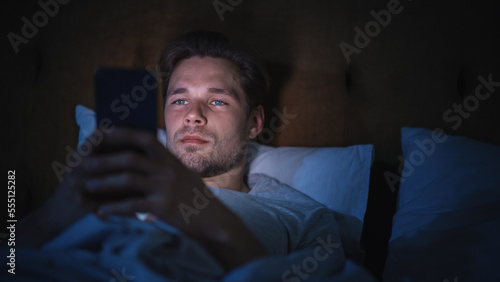 Caucasian Man Uses Smartphone in Bed at Home at Night. Handsome Guy Browsing Social Media, Reading News, Doing Online Shopping, Chatting with Friends Late at Night.