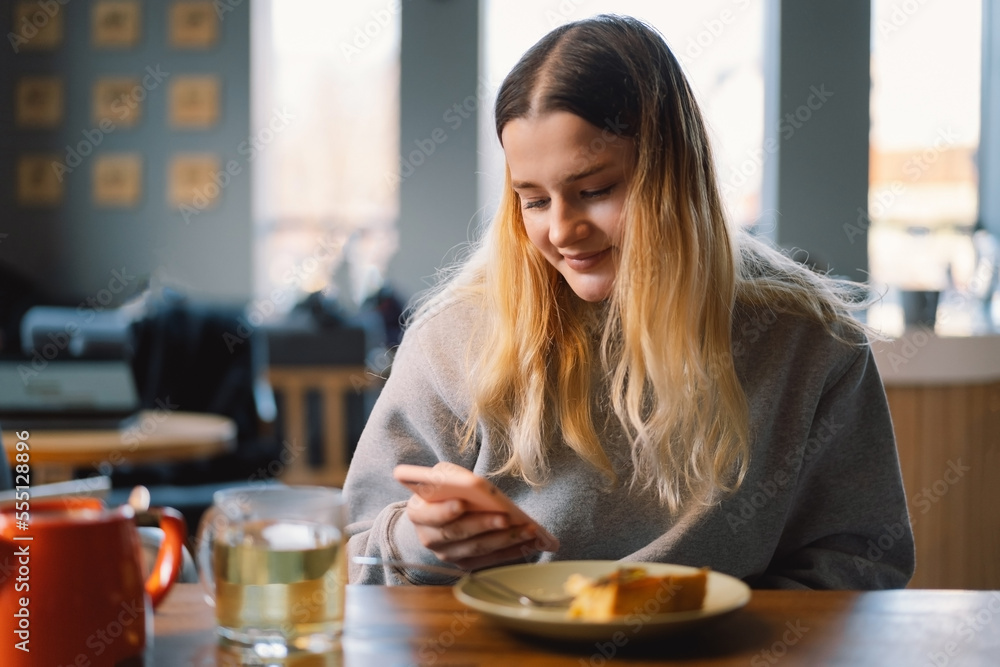 A young girl in a cafe uses the phone. People use technology. Cafe city lifestyle. Colorful portrait of happy pretty girl. A young girl in a cafe uses the phone. People use technology. Cafe city lifestyle. Colorful portrait of happy pretty girl.