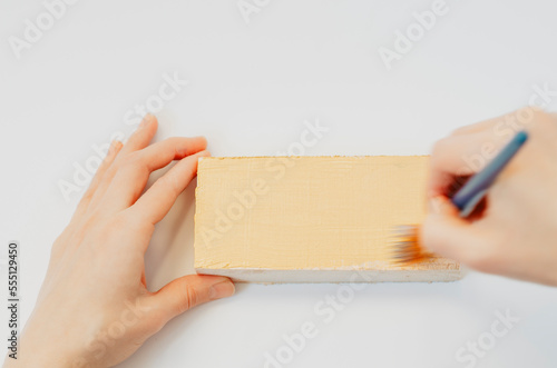 Hands painting a piece of wood with pale yellow acrylics on white background © Cristina