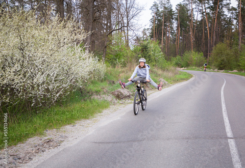 happy woman in a helmet rides a bicycle along an asphalt road through the forest along flowering trees. energy of nature, rest, freedom, travel. Active healthy lifestyle © Anna