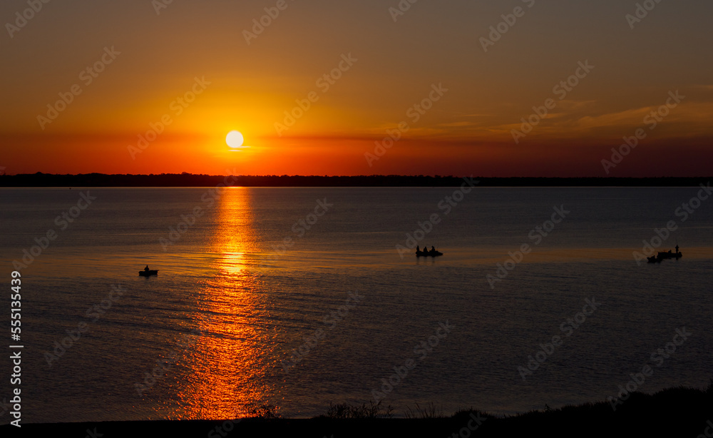 sunset over the sea or estuary in red-orange warm colors with a sunny path on the water, ripples and waves on the water, boats with fishermen in Ukraine in Europe sunset over the sea or estuary in red-orange warm colors with a sunny path on the water, ripples and waves on the water, boats with fishermen in Ukraine in Europe