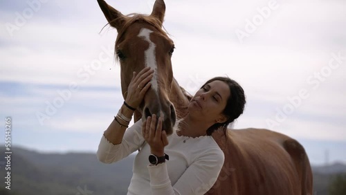 Brunette woman kisses and plays with a brown horse while walking in the field. Friendship, love and care between horses and people. Brown horse on a farm