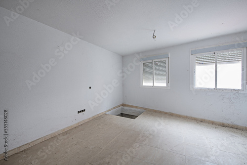 A room with aluminum windows and a hole in the floor that must be finished to finish the electrical installation