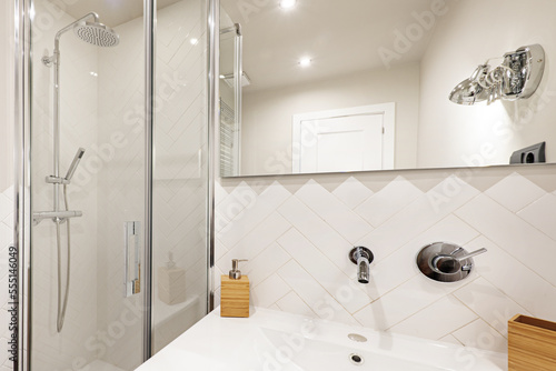 White tiled toilet with designer faucets and walk in shower with glass partition and frameless mirror on the wall