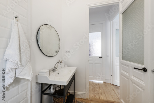 Vintage-style bathroom with porcelain sink on metal cabinet, circular mirror and solid wood door with translucent glass © Toyakisfoto.photos