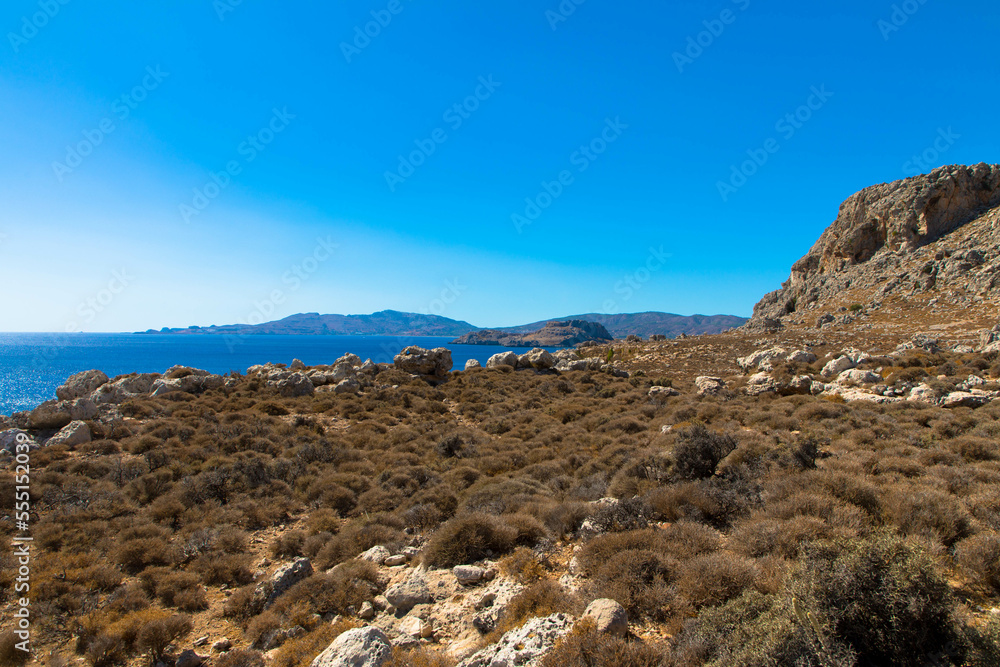 Panoramic view of the Mediterranean Sea on the rocky coast. Mountain range with clear turquoise water and blue sky. Located near Stegna, Archangelos, Rhodes, Dodecanese Islands, Greece