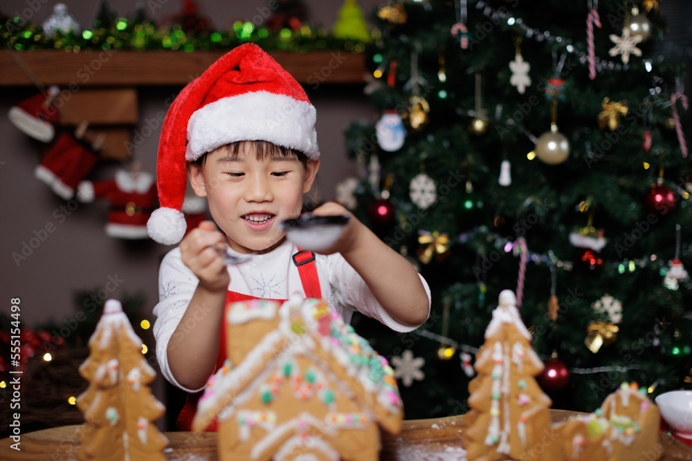 young girl wearing Santa hat was decorating gingerbread house for celebrating Christmas at home young girl wearing Santa hat was decorating gingerbread house for celebrating Christmas at home
