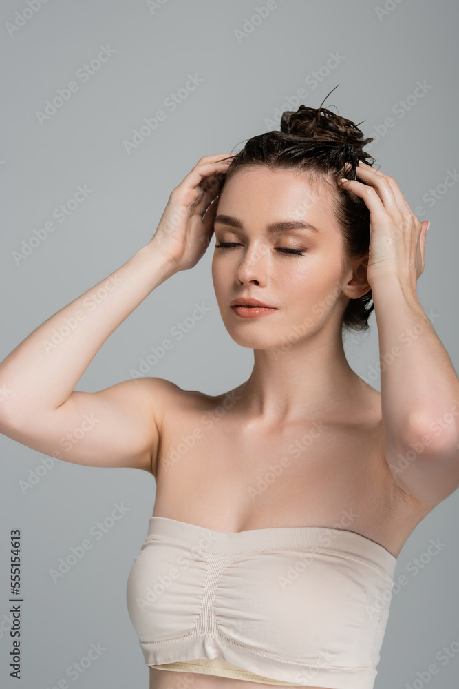 pretty young woman with closed eyes washing hair isolated on grey