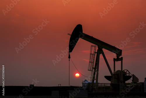 Silhouette of pumpjack with a glowing warm sun ball in the background, West of Airdrie; Alberta, Canada