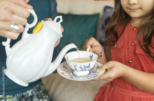 A mother pouring tea into a teacup with saucer for her daughter; Surrey, British Columbia, Canada photo