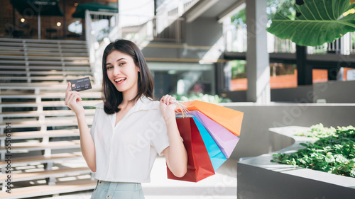 Woman smiling and holding a brightly colored shopping bag while walking through a shopping mall., Moments of happiness for ladies.