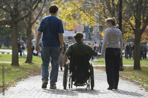 Rear view of a man sitting in a wheelchair with a man and a woman walking to a war protest photo