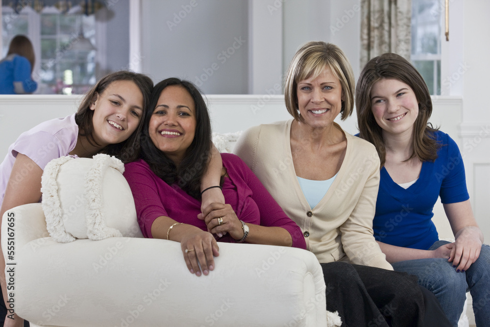 Two mothers with their daughters sitting on a couch in a home Two mothers with their daughters sitting on a couch in a home