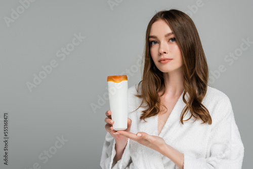 young woman with shiny hair holding bottle with shampoo isolated on grey photo