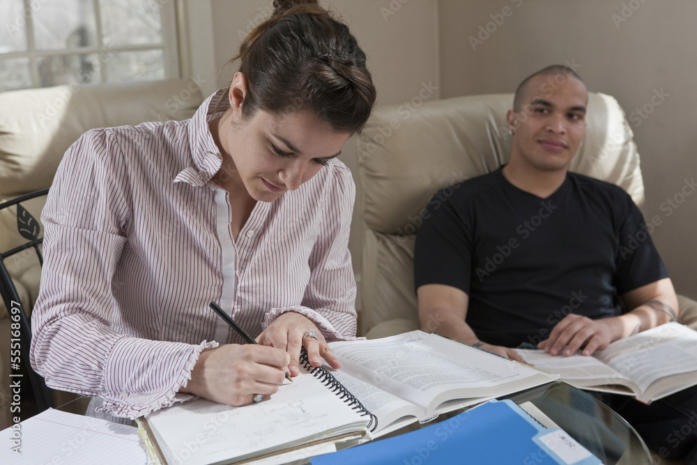 Female college student doing homework at home while boyfriend looks on in encouragement Female college student doing homework at home while boyfriend looks on in encouragement