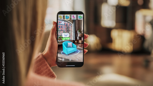 Decorating Apartment: Woman Holding Smartphone, using Augmented Reality Interior Design Software Chooses 3D Furniture for Home. Pick a Stylish Chair for the Living Room. Over Shoulder Close-up Screen
