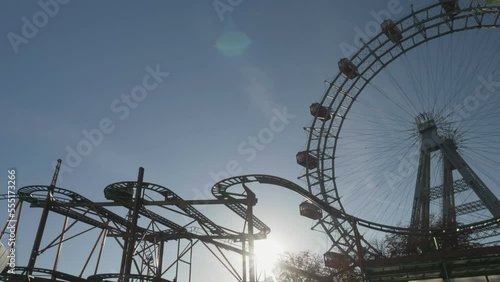 Sun behind roller coaster and Ferris wheel in the amusement park photo