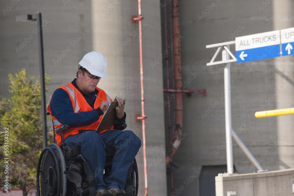 Facilities engineer in a wheelchair inspecting outdoor bulk storage tanks and recording data Facilities engineer in a wheelchair inspecting outdoor bulk storage tanks and recording data