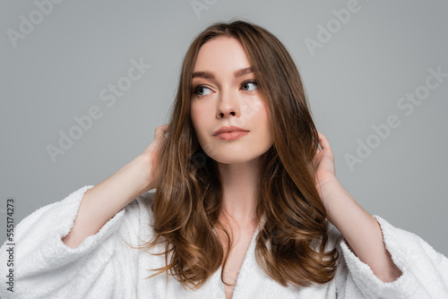 Obraz na plátně young woman in bathrobe touching shiny and healthy hair while looking away isola
