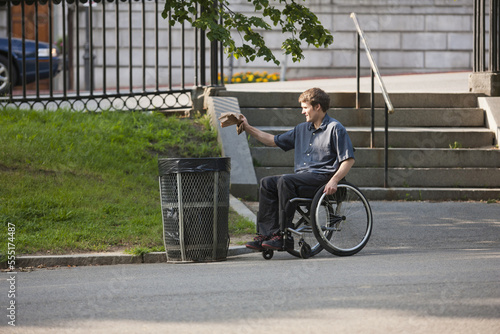 Man with spinal cord injury in a wheelchair putting trash in receptacle at public park photo