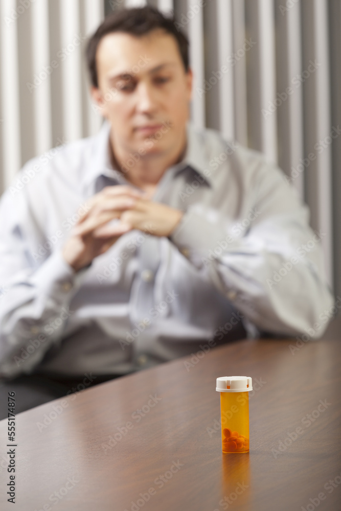 Businessman at desk looking at a pill bottle Businessman at desk looking at a pill bottle
