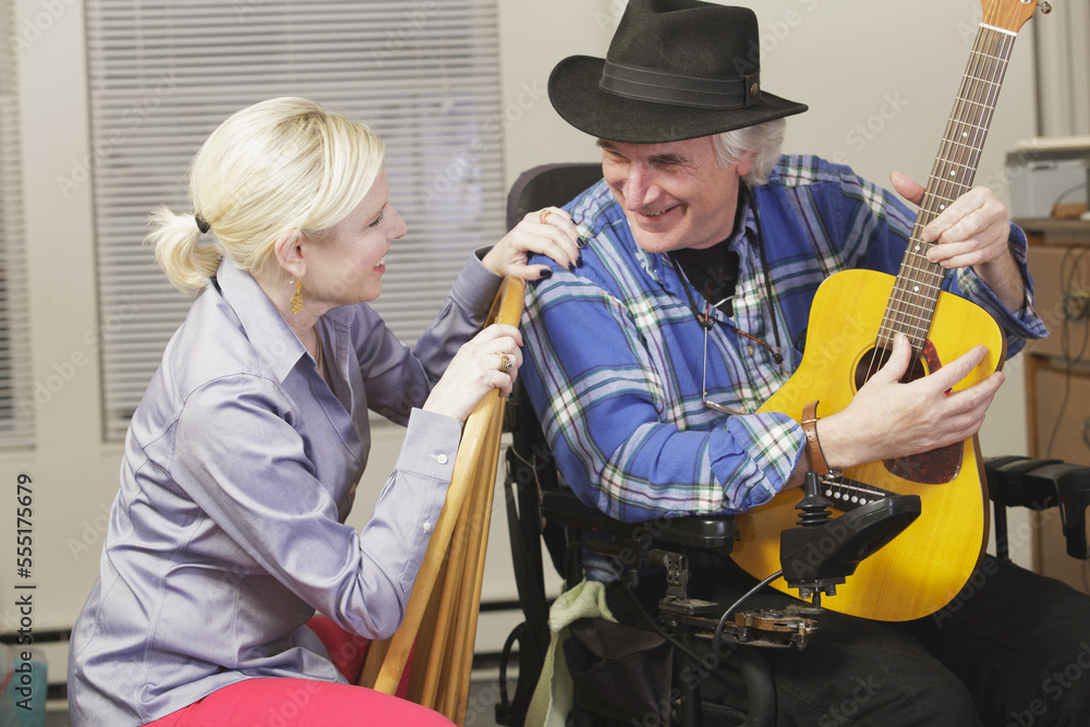Musician with Multiple Sclerosis in a motorized wheelchair with his guitar playing for a friend Musician with Multiple Sclerosis in a motorized wheelchair with his guitar playing for a friend