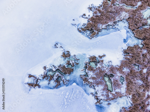 Aerial view of frozen swamp with dry grass and blue green ice.