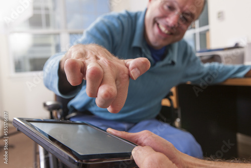 Two disabled men sitting in wheelchairs and using a digital tablet, one with deformed hands photo
