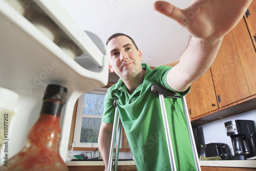 Man after anterior cruciate ligament (ACL) surgery with crutches reaching in his refrigerator in the kitchen photo