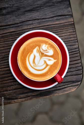 A cup of cappuccino with rose on top on wooden table