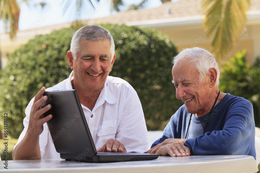 Elderly man, who is visually impaired, using a laptop with his son beside him Elderly man, who is visually impaired, using a laptop with his son beside him