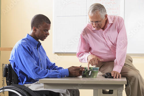 Professor and engineering student in wheelchair looking at a circuit board with LCD display photo