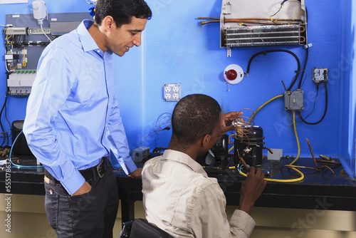 Students examining condenser coil on refrigeration unit in HVAC classroom